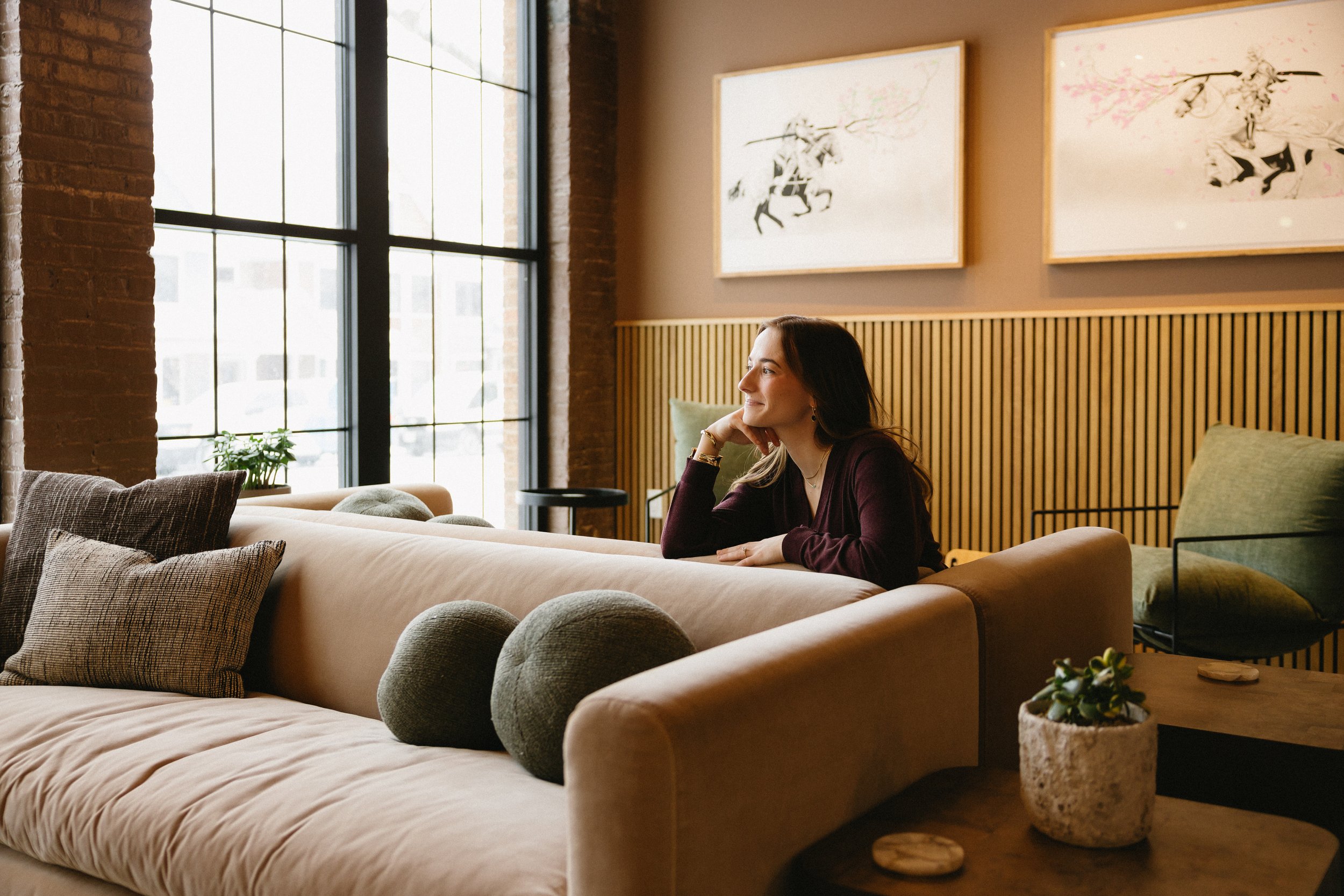 Jade Hartley seated in The Dylin lounge beside large windows, with framed artwork behind her.