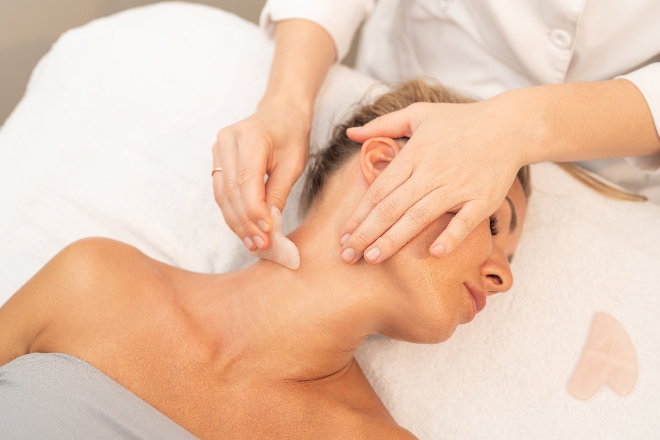 Esthetician performing gua sha facial massage on client's neck