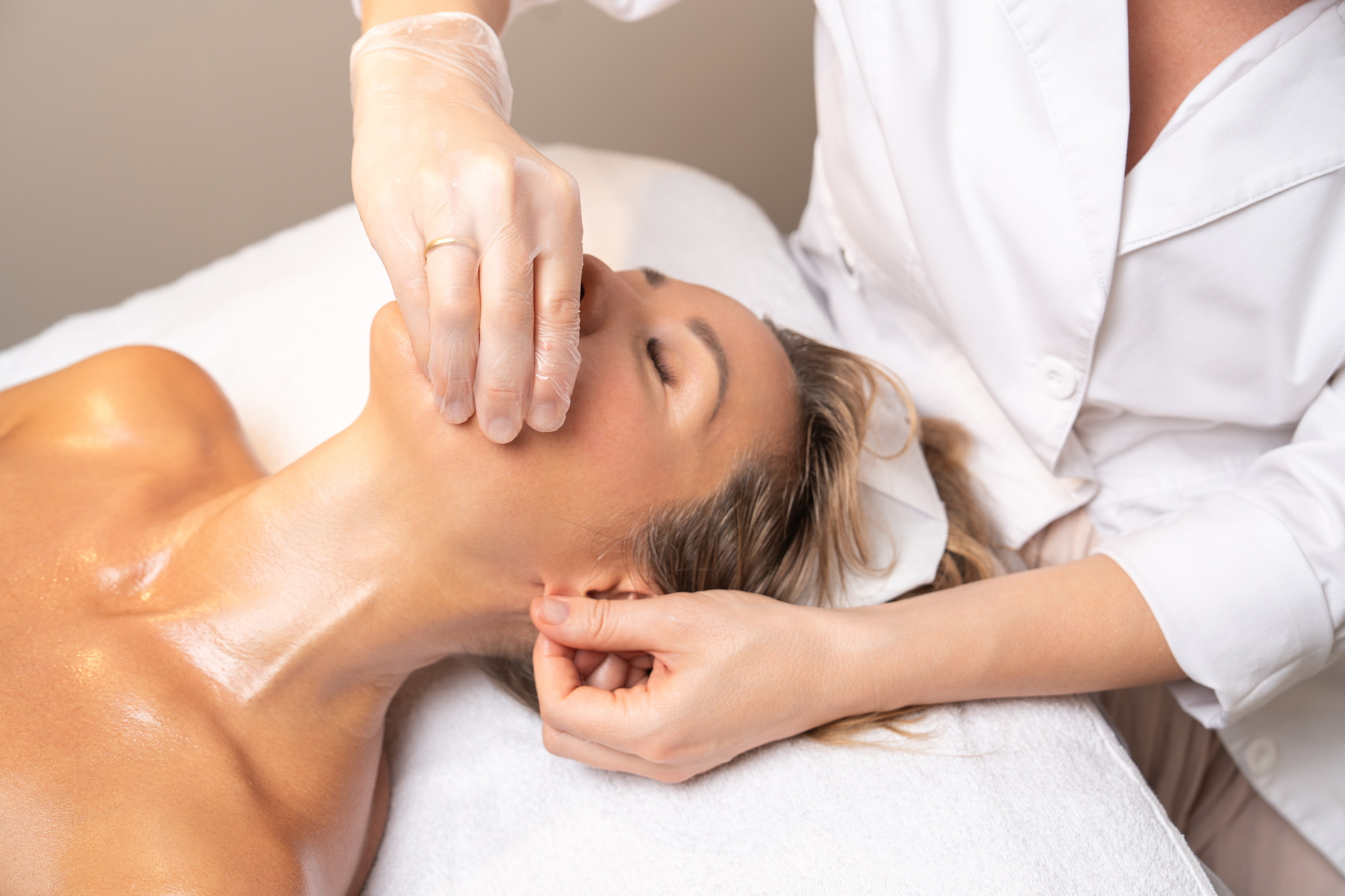 Esthetician massaging client's jaw with gloved hands during buccal massage