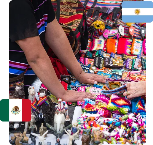 Hands of two people browsing colorful handmade crafts and figurines at a market stall.