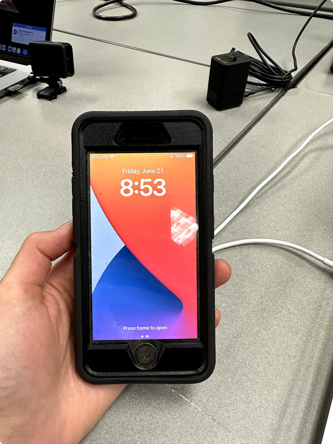Hand holding a black-cased iPhone showing lock screen with date June 21 and time 8:53.