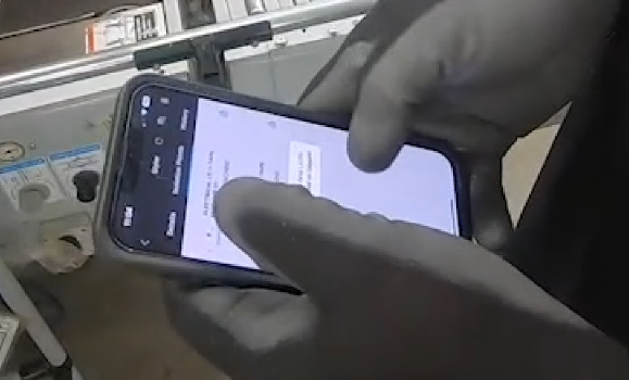 Person in black gloves holding smartphone over machinery in an industrial setting.