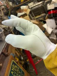 Hand wearing a white protective glove with a yellow sleeve in a workshop setting.