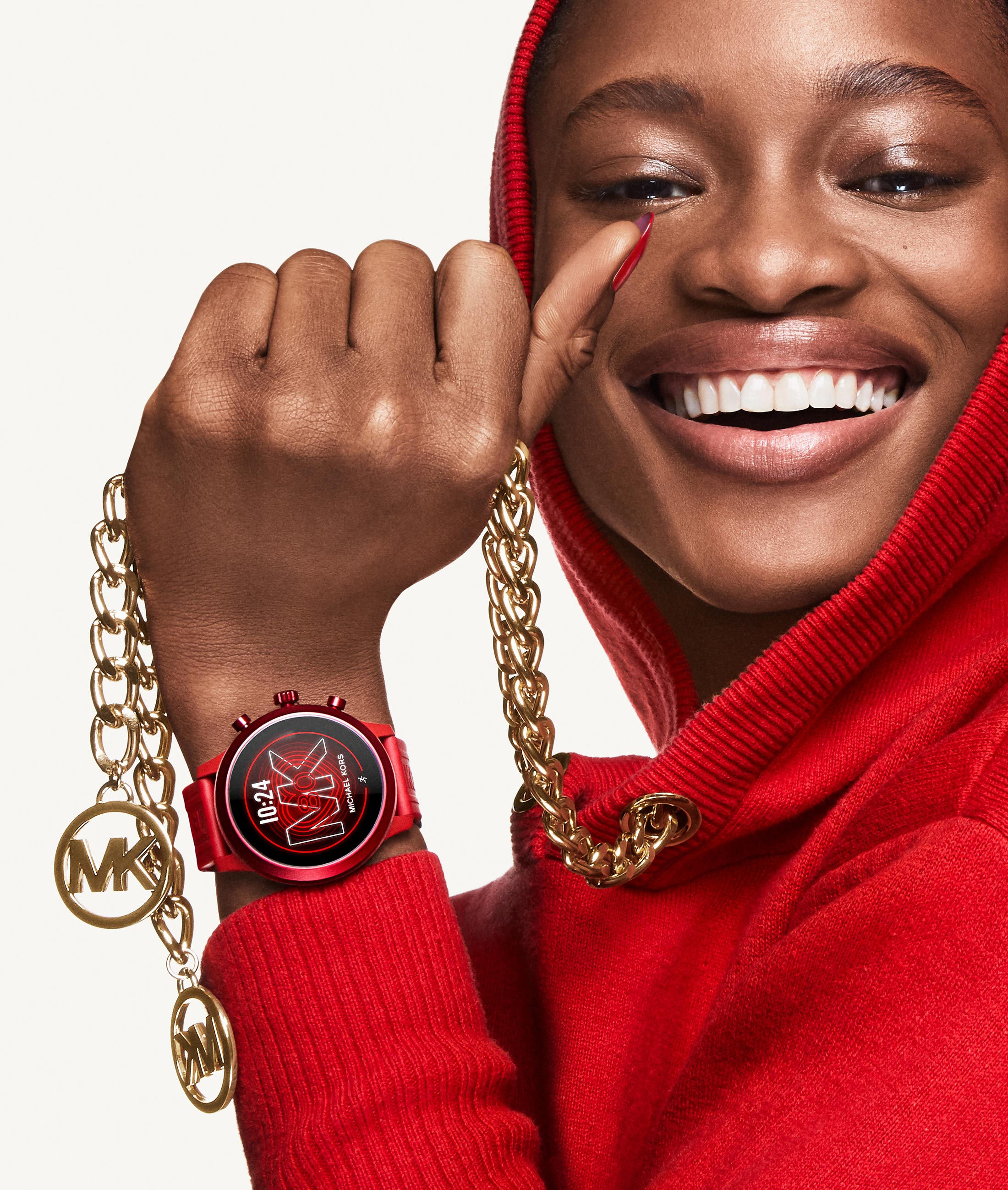 Smiling person in red hoodie showing a red Michael Kors watch and holding a gold chain with MK logos.