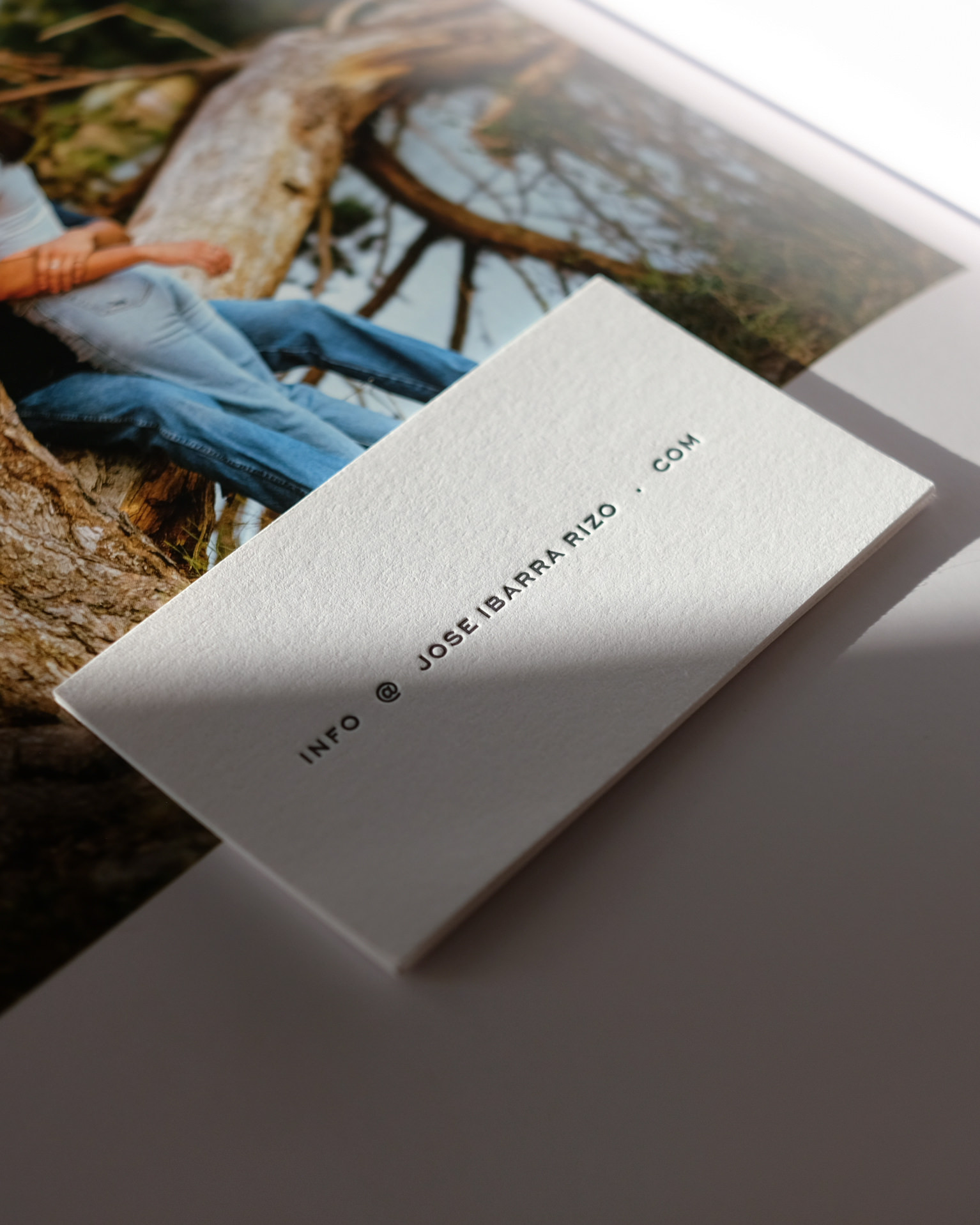 Close-up of a white card with text 'INFO @ JOSE IBARRA RIZO . COM' on a surface with a photo background.