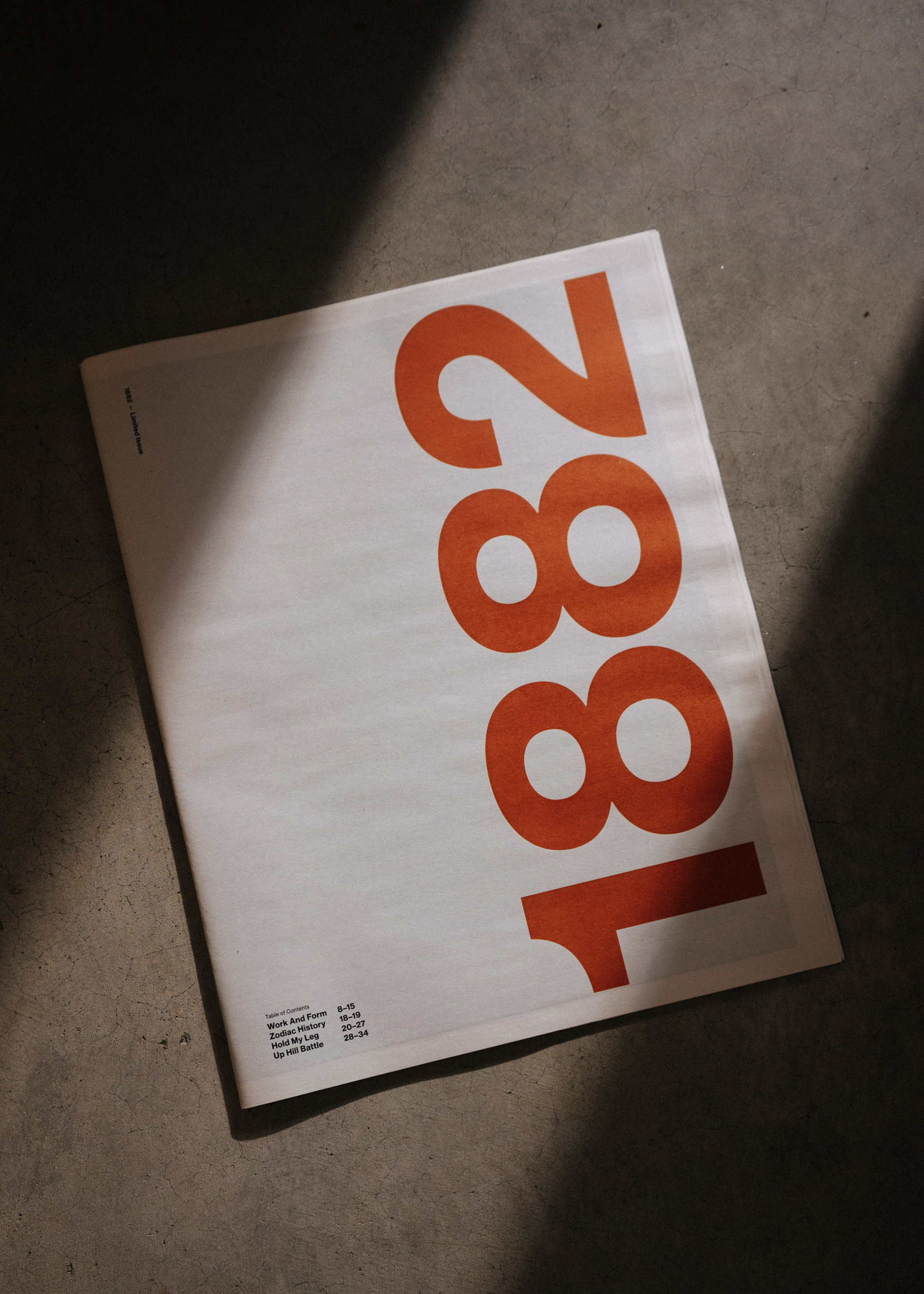 Newspaper on concrete floor with large orange numbers 1882 and a table of contents in corner.