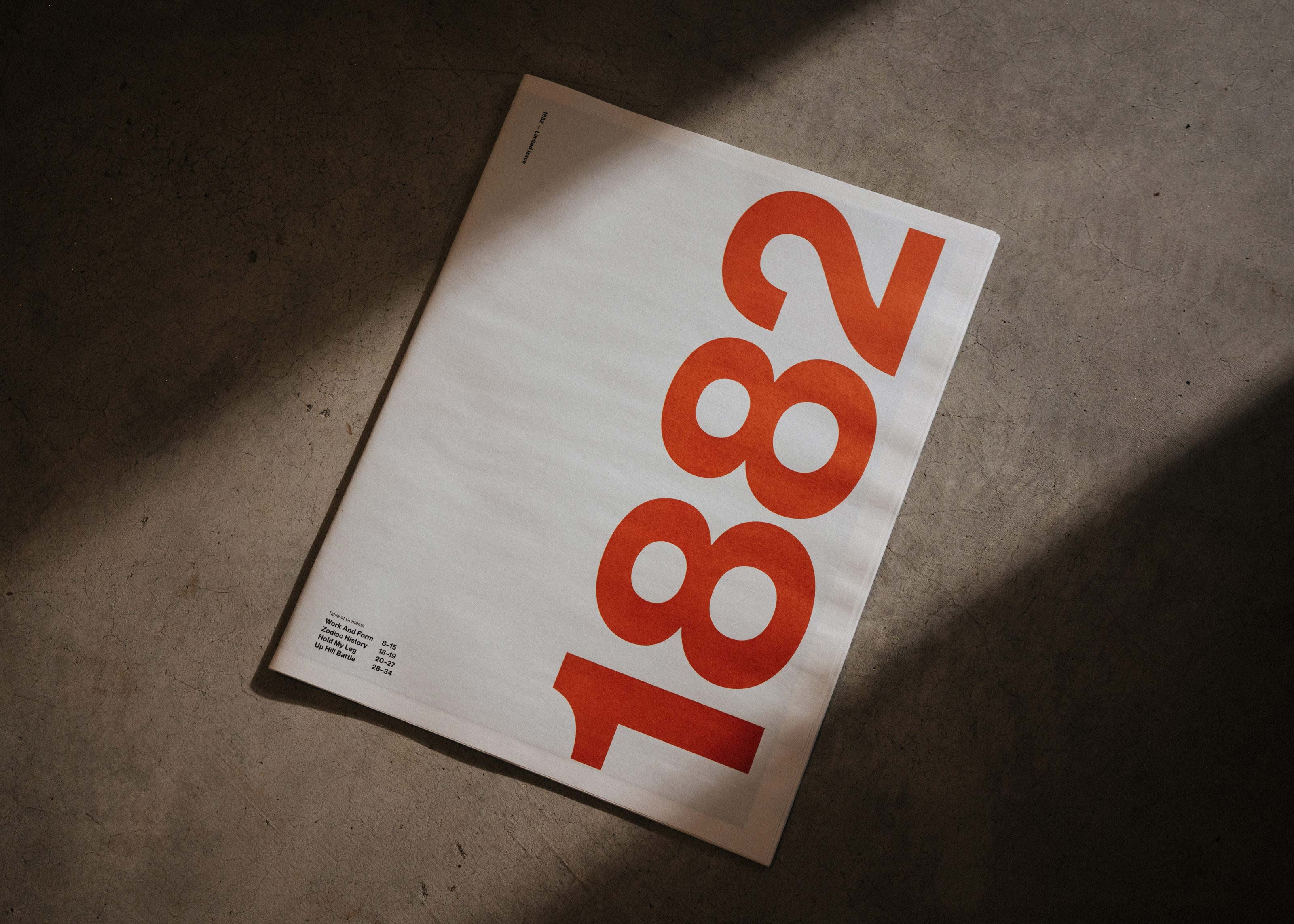White magazine with large orange numbers 1882 on the cover lying on a concrete floor.