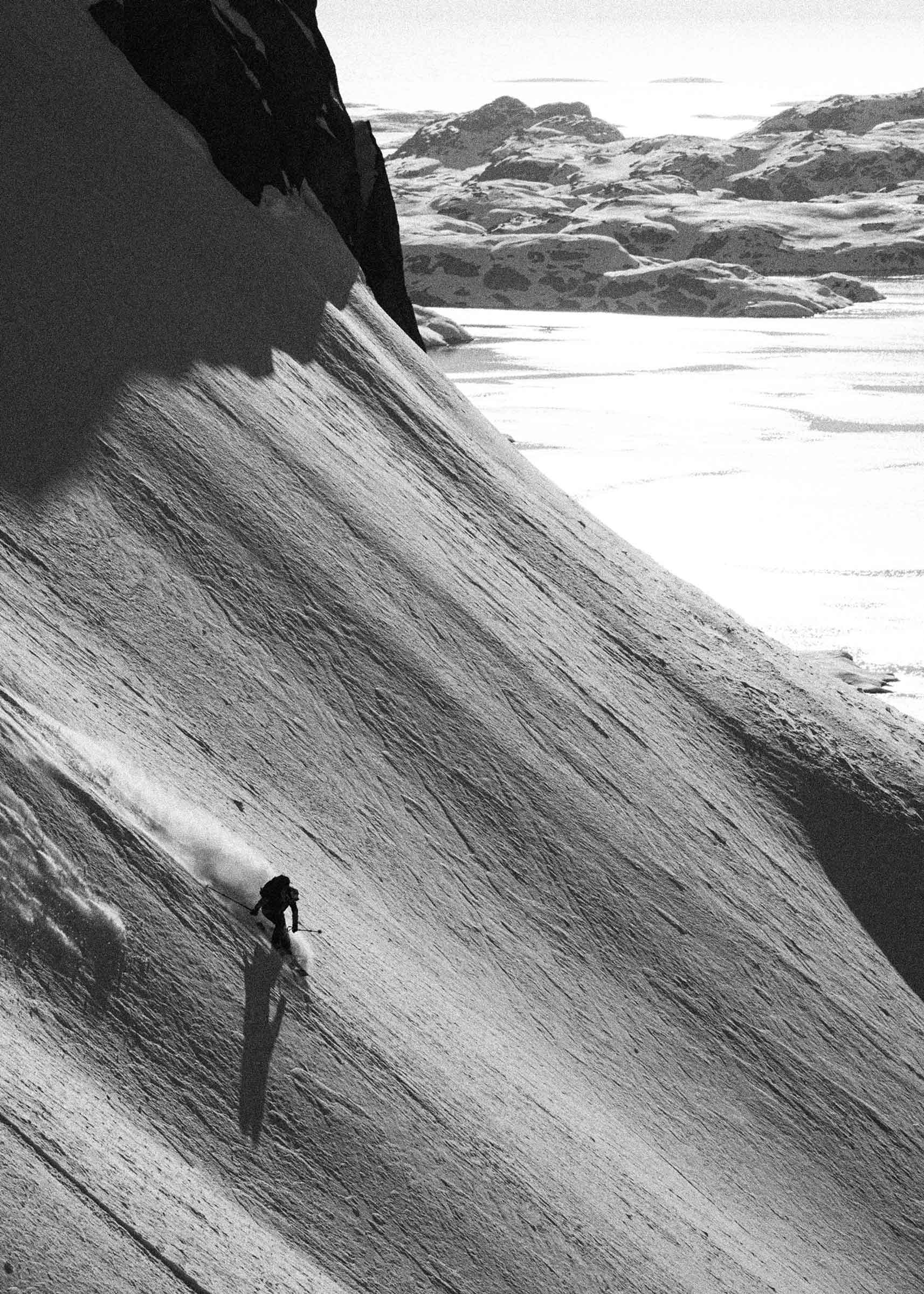 Skier descending a steep snowy mountain slope with rocky snow-covered peaks in the background.