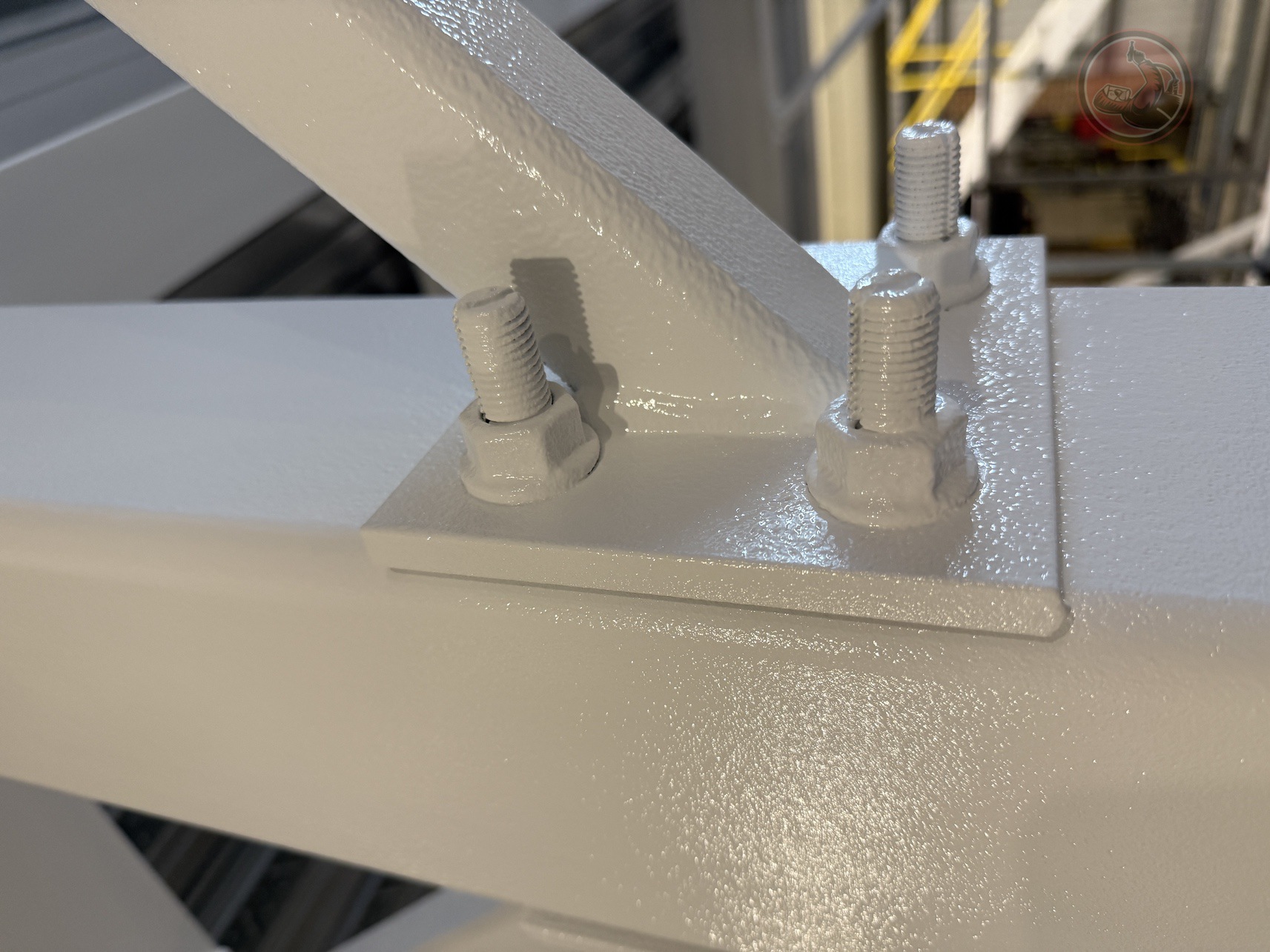 Close-up of a white-painted metal bracket with bolts securing a diagonal support beam to a vertical column in an industrial setting.