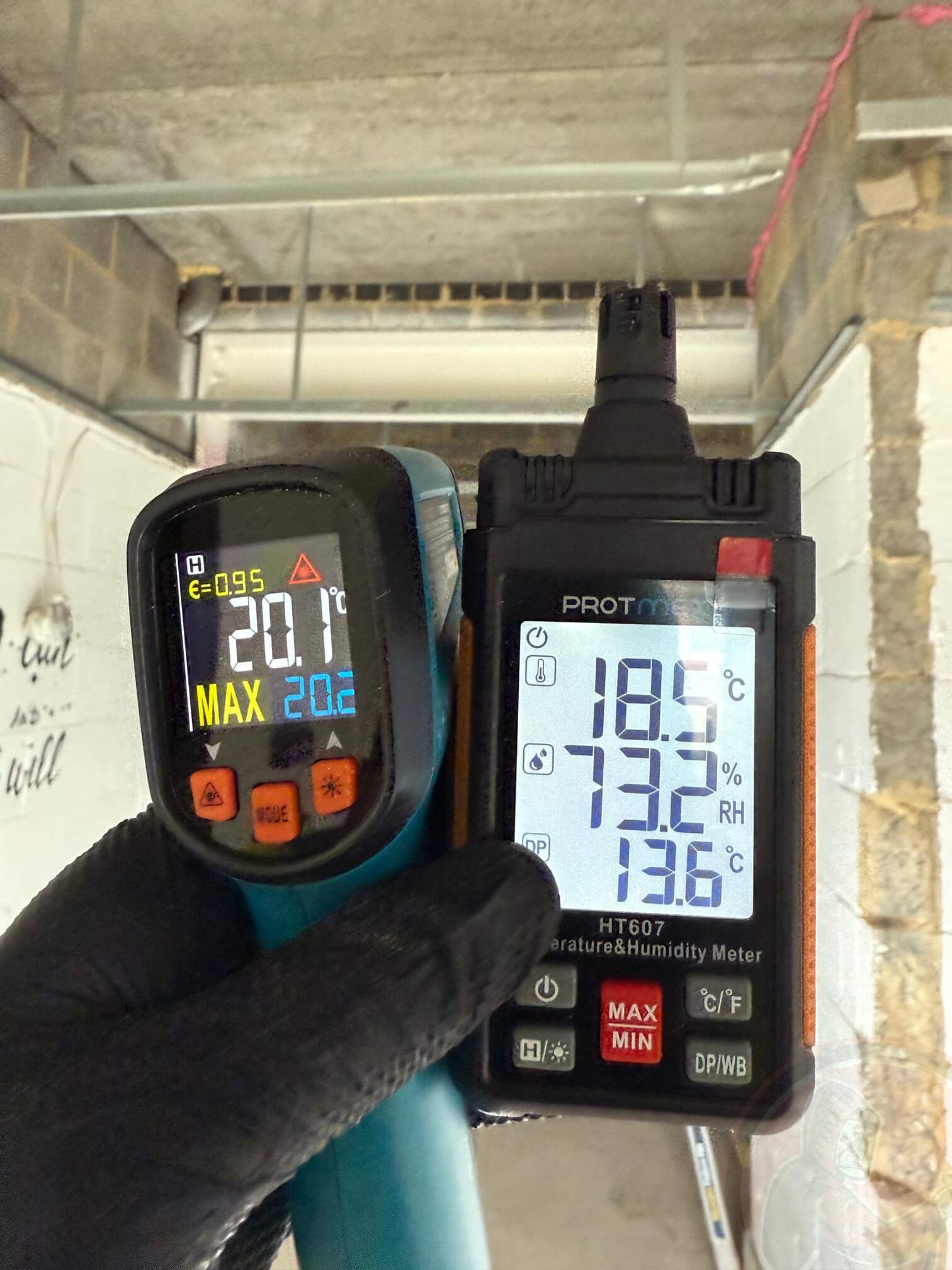 Hand in black glove holding two temperature and humidity measuring devices showing 20.1°C and 18.5°C with 73.2% humidity.