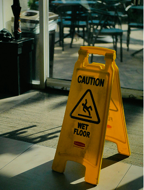 Yellow caution sign indicating a wet floor placed on a carpeted floor near glass doors.