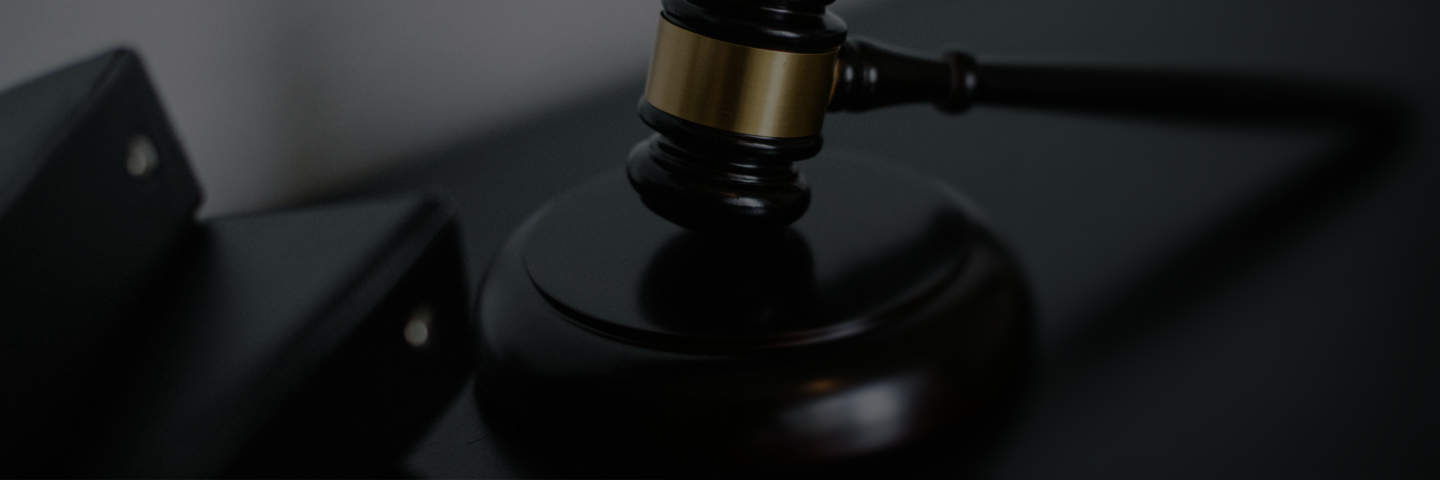 Close-up of a wooden judge's gavel resting on a sound block with black legal binders in the background.