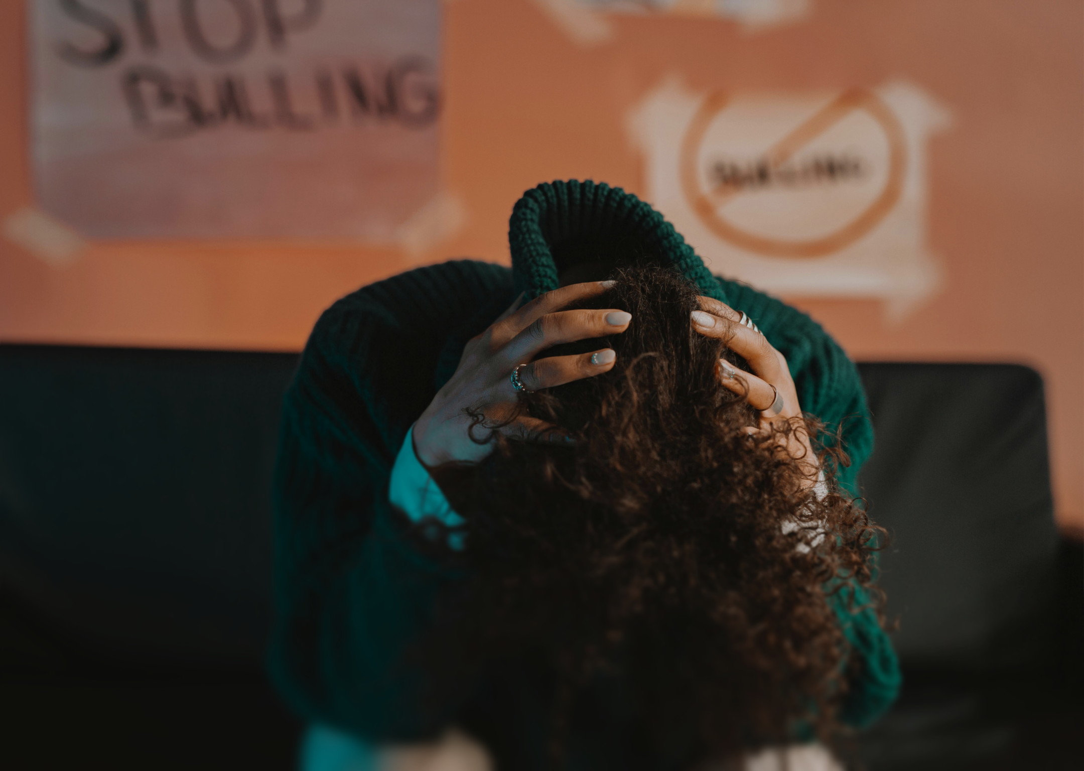 Person with curly hair sitting with their head in their hands in front of anti-bullying posters.