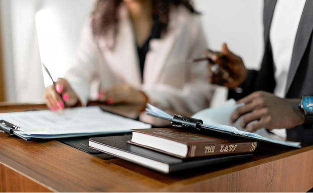 Two people reviewing legal documents at a wooden desk with a law book and binder in the foreground.
