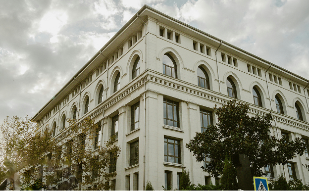 Corner view of a white, multi-story classical building with arched windows and a cloudy sky above.