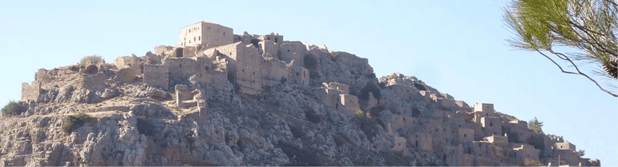 Ruins of an ancient stone fortress built on a rocky hill under a clear blue sky.