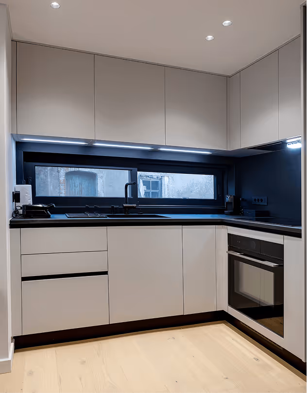 Modern minimalist kitchen with white cabinets, black countertops, a built-in oven, and under-cabinet lighting.