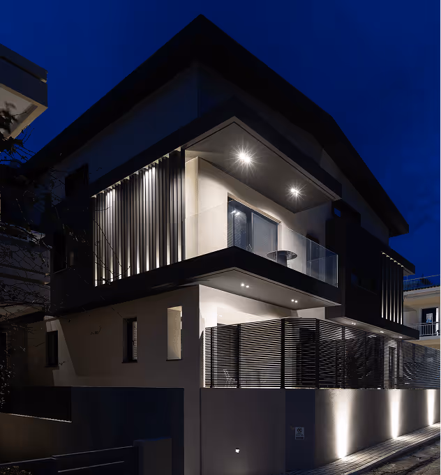 Modern two-story house illuminated at night with balcony and vertical slatted exterior design.