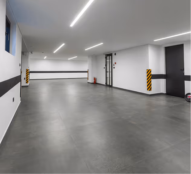 Empty indoor parking garage with gray floor and white walls marked with black stripes and corner protectors.