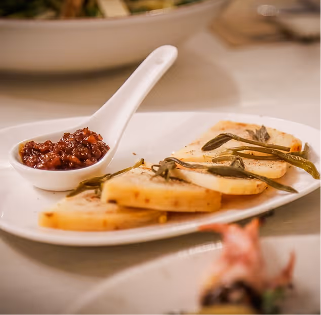 White plate with several slices of grilled or roasted cheese garnished with herbs and a white spoon containing a red chutney or sauce.