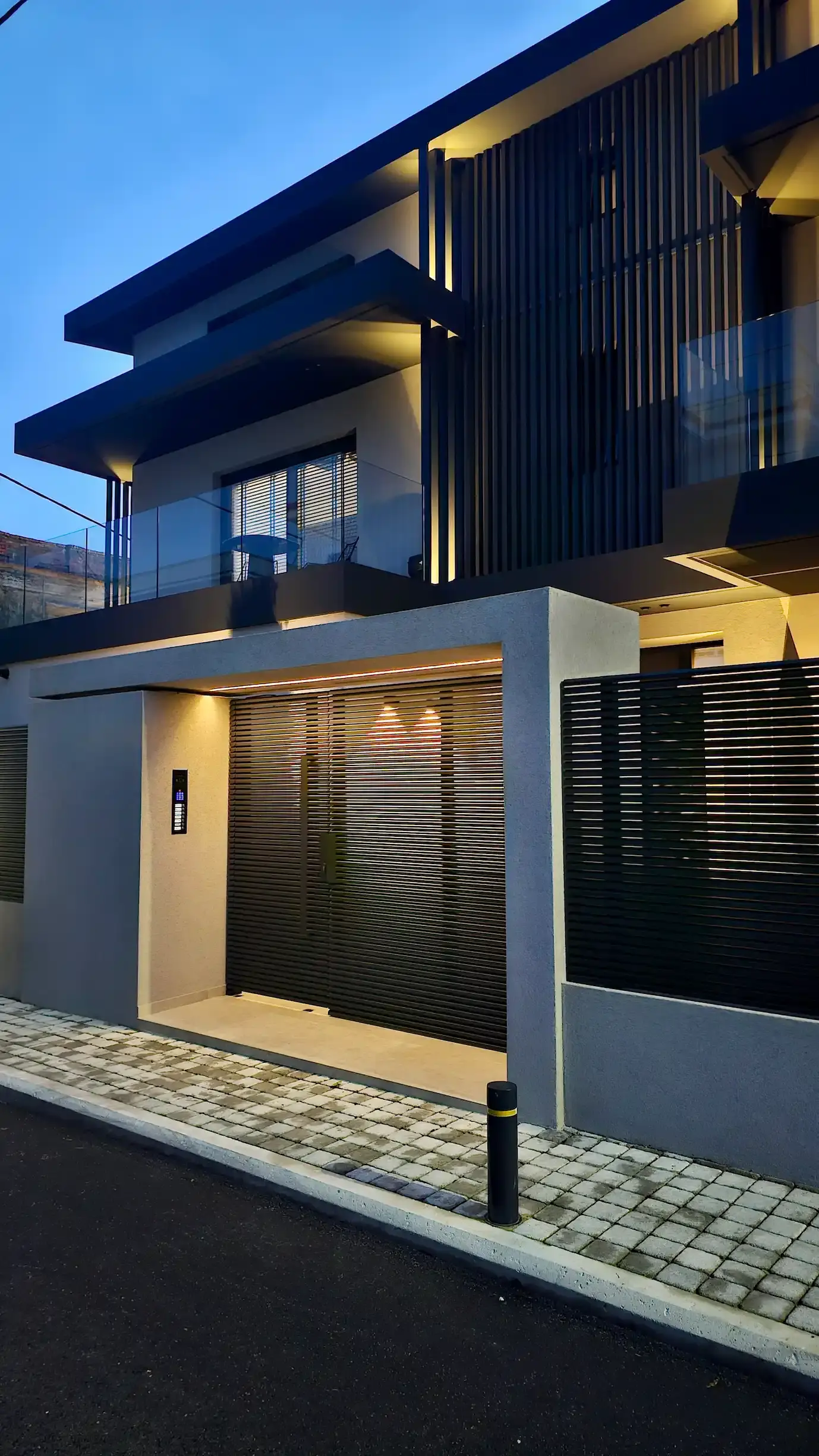 Modern living room viewed from above with circular pendant lights, a gray sofa, black rug, white kidney-shaped coffee table, and large window blinds.