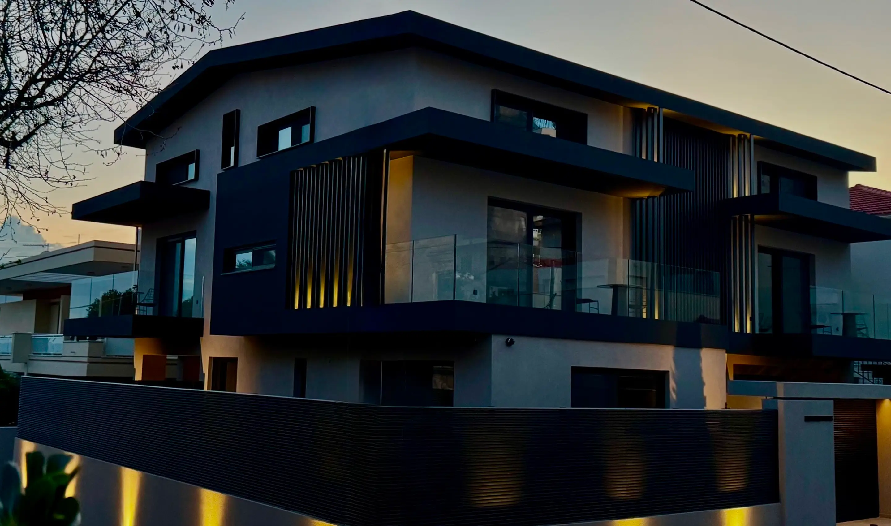 Modern two-story house exterior at dusk with warm lighting and glass balcony railings.
