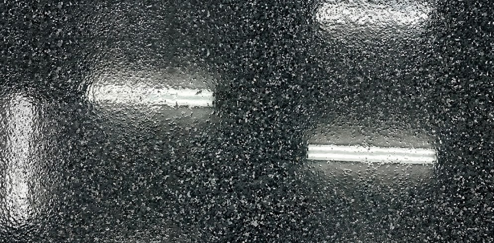 Close-up of textured black surface with scattered small white flakes and reflections of overhead lights.