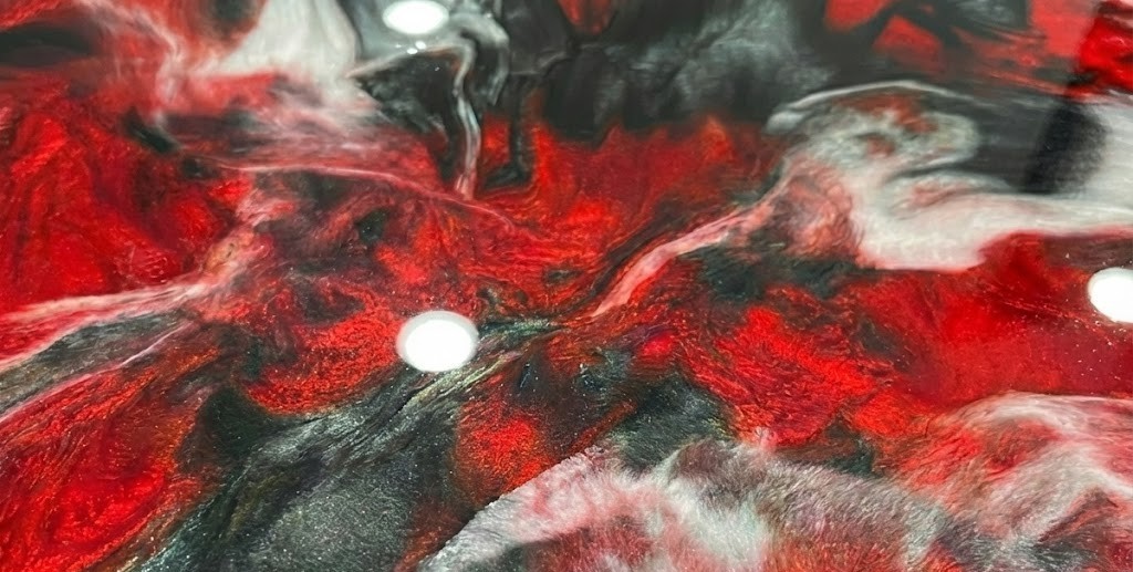 Glossy surface with swirling red, black, and white metallic colors creating a marbled effect.