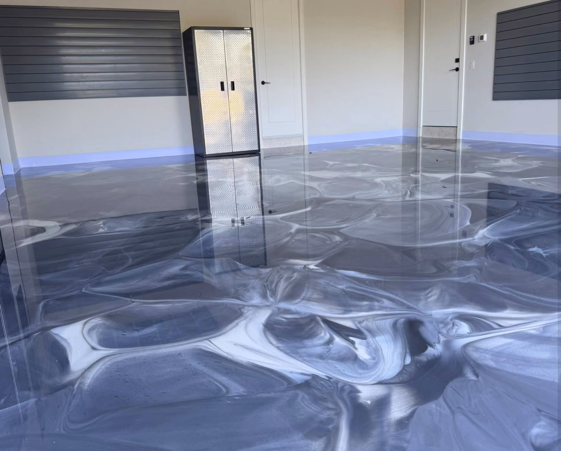 Garage interior with shiny, marbled black and white epoxy floor and a metal storage cabinet against a beige wall.