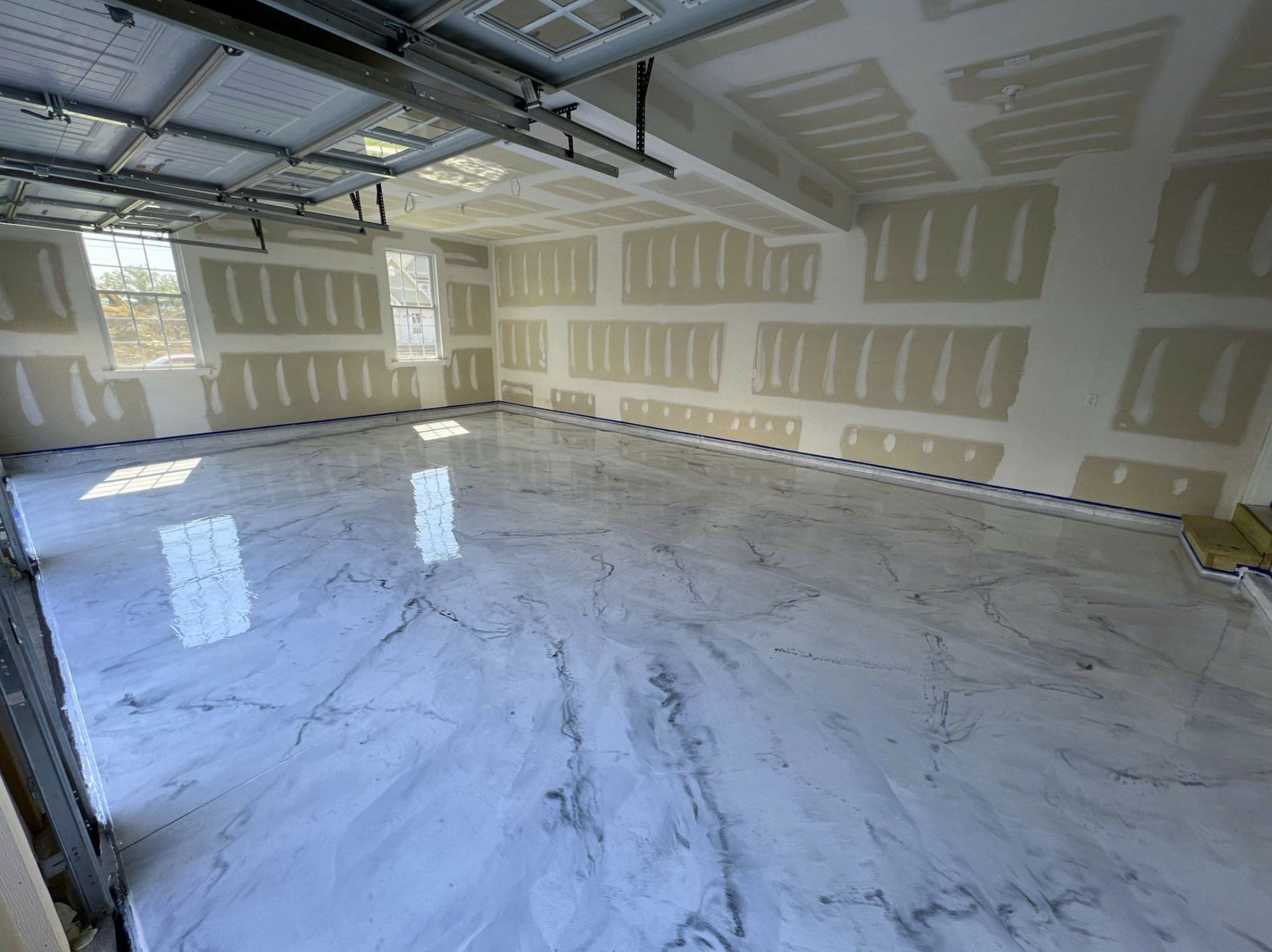 Empty unfinished garage with white and gray marbled epoxy floor and drywall walls with taped seams.