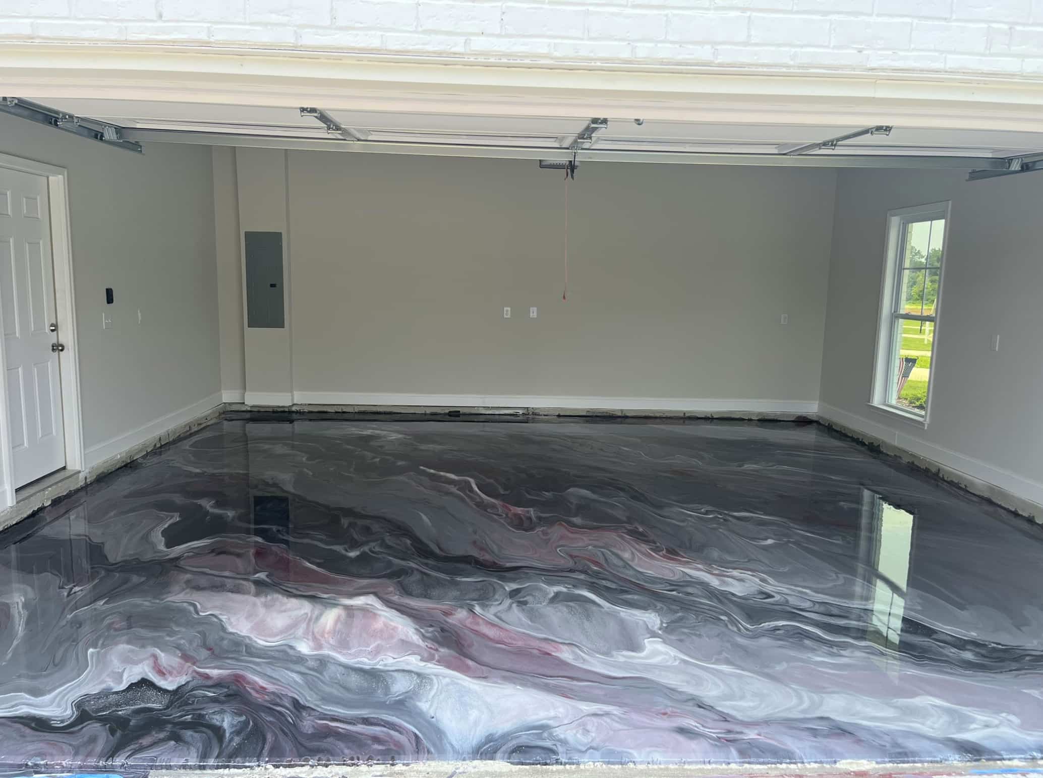 Empty garage with a high-gloss epoxy floor featuring a swirling marbled pattern in black, gray, white, and hints of red.