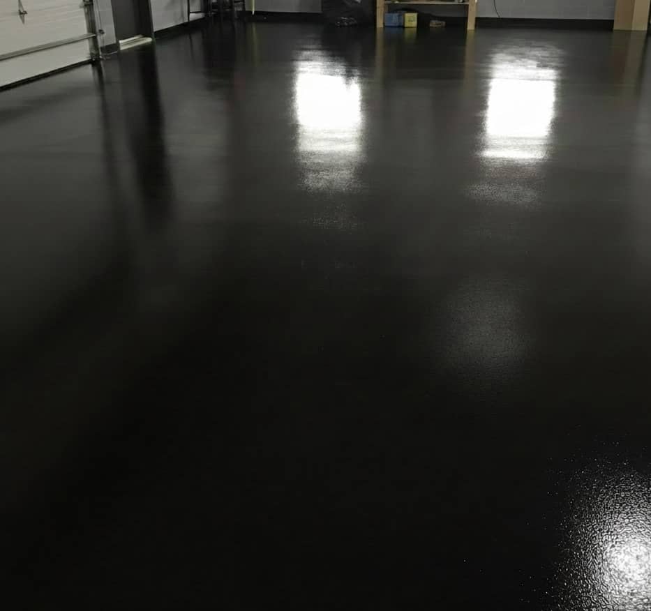 Shiny black epoxy-coated garage floor reflecting overhead lights inside a clean garage.