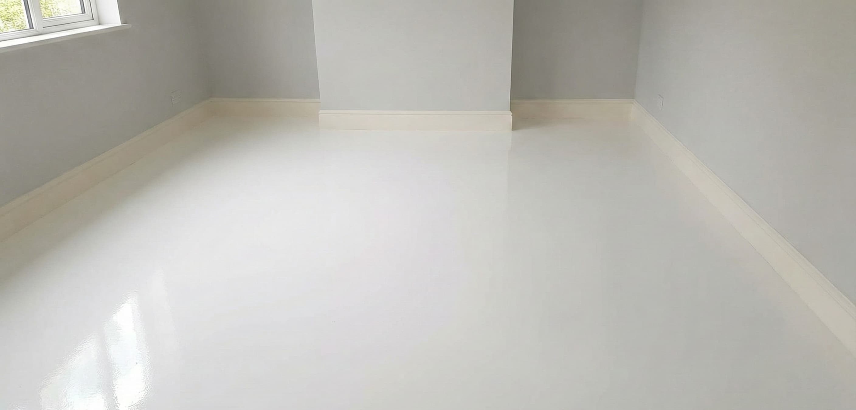 Empty room with smooth, glossy white floor, light gray walls, and white baseboards with a window on the left.