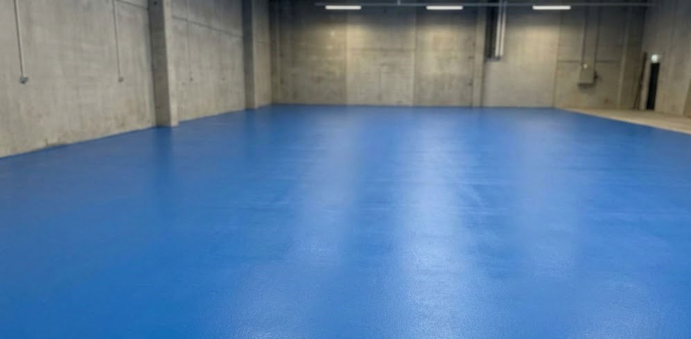 Empty indoor space with blue epoxy floor and gray concrete walls.