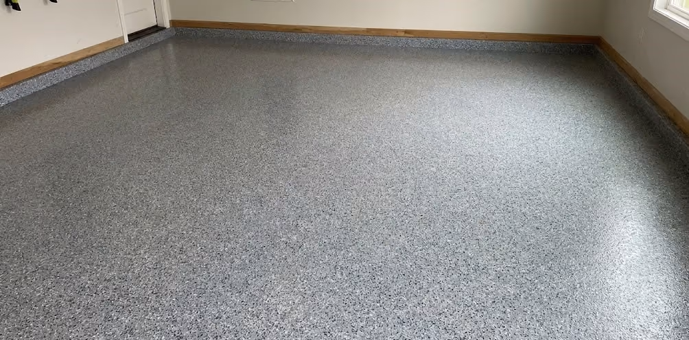 Empty garage with clean, speckled gray epoxy floor and white walls with wooden trim.