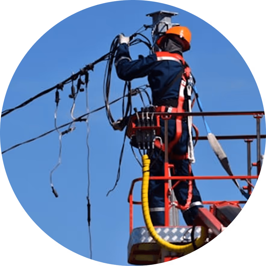 Elektriker mit Schutzhelm und Sicherheitsausrüstung arbeitet an Kabeln auf einer Hebebühne vor blauem Himmel.