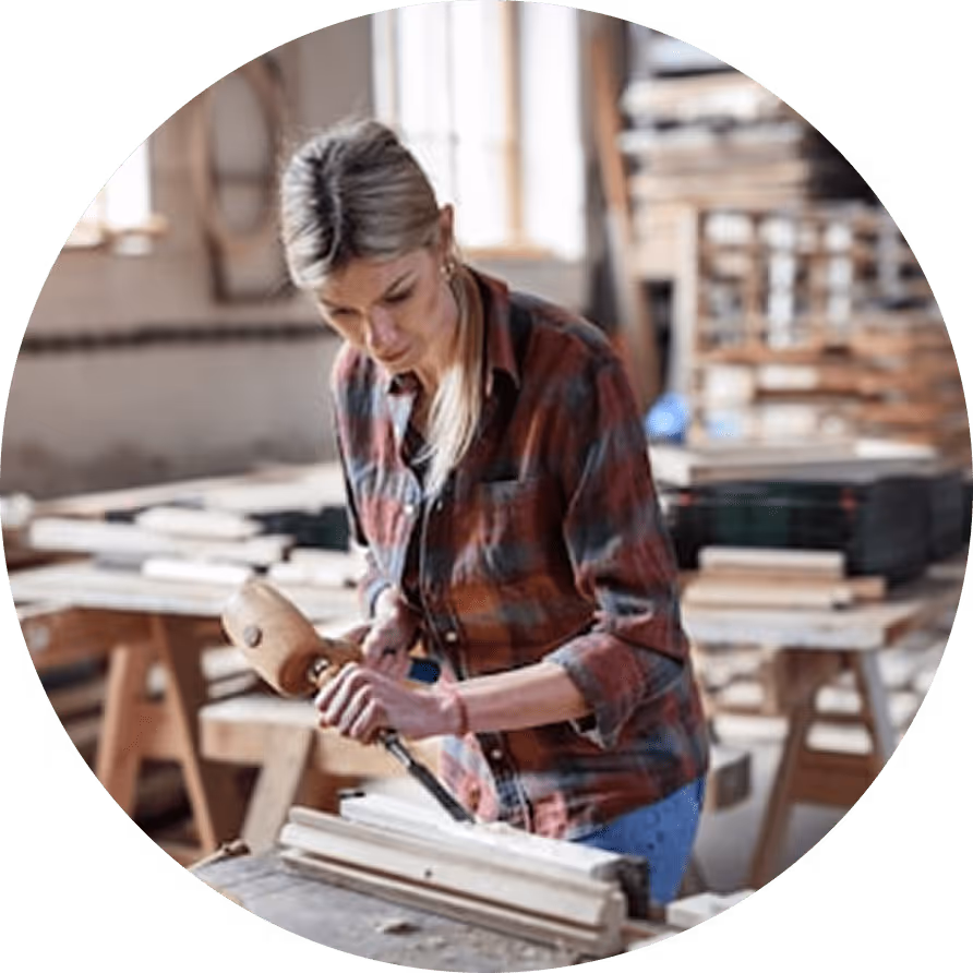 Eine Frau benutzt einen Hammer und Meißel, um Holz in einer Werkstatt zu bearbeiten.