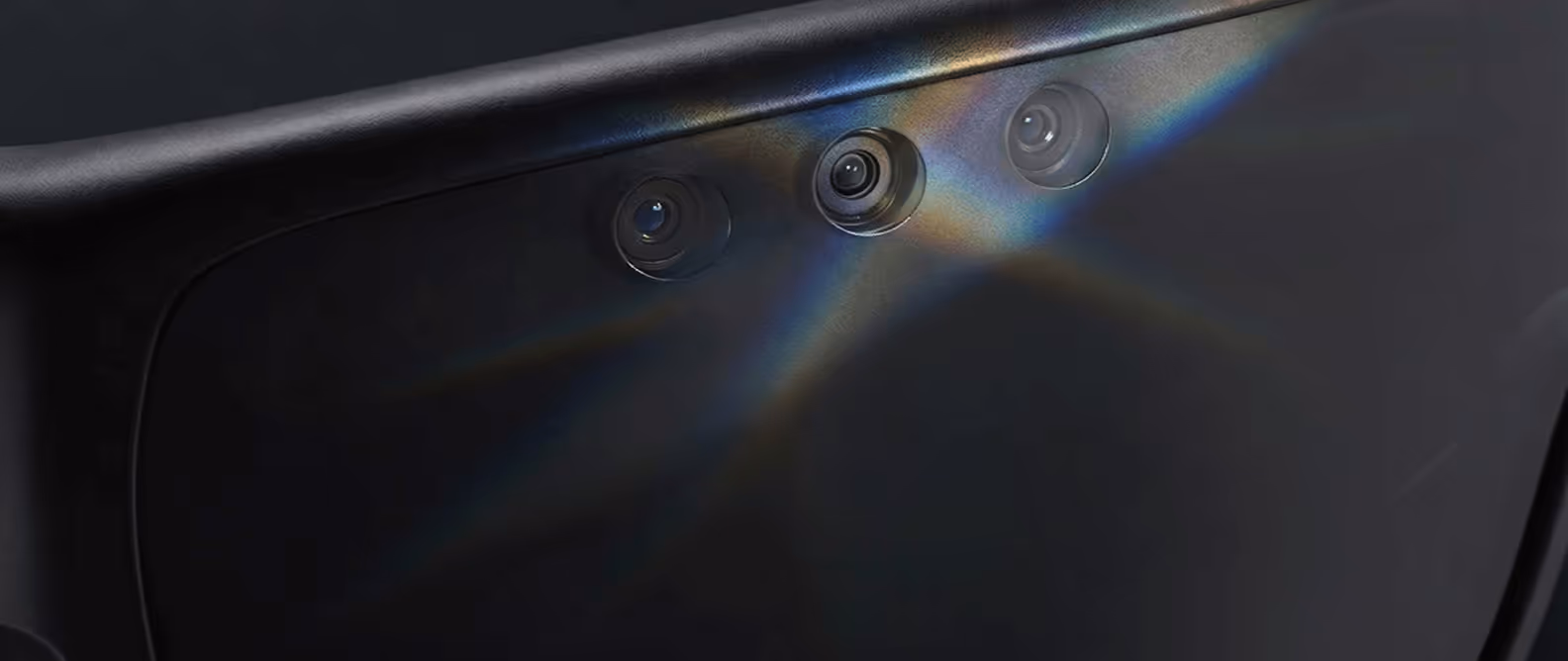 Close-up of three camera lenses on a dark electronic device with light reflections.