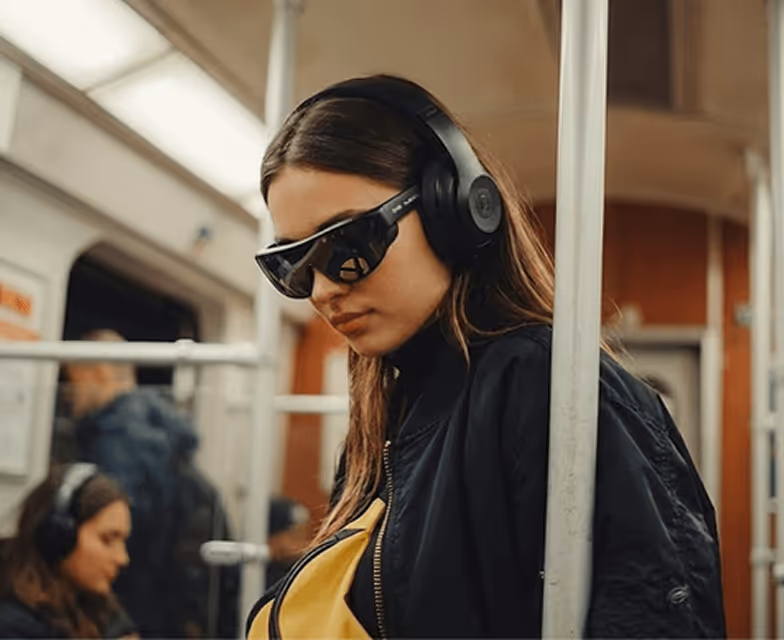 Young woman wearing black headphones and Mixverse sunglasses inside a subway train.