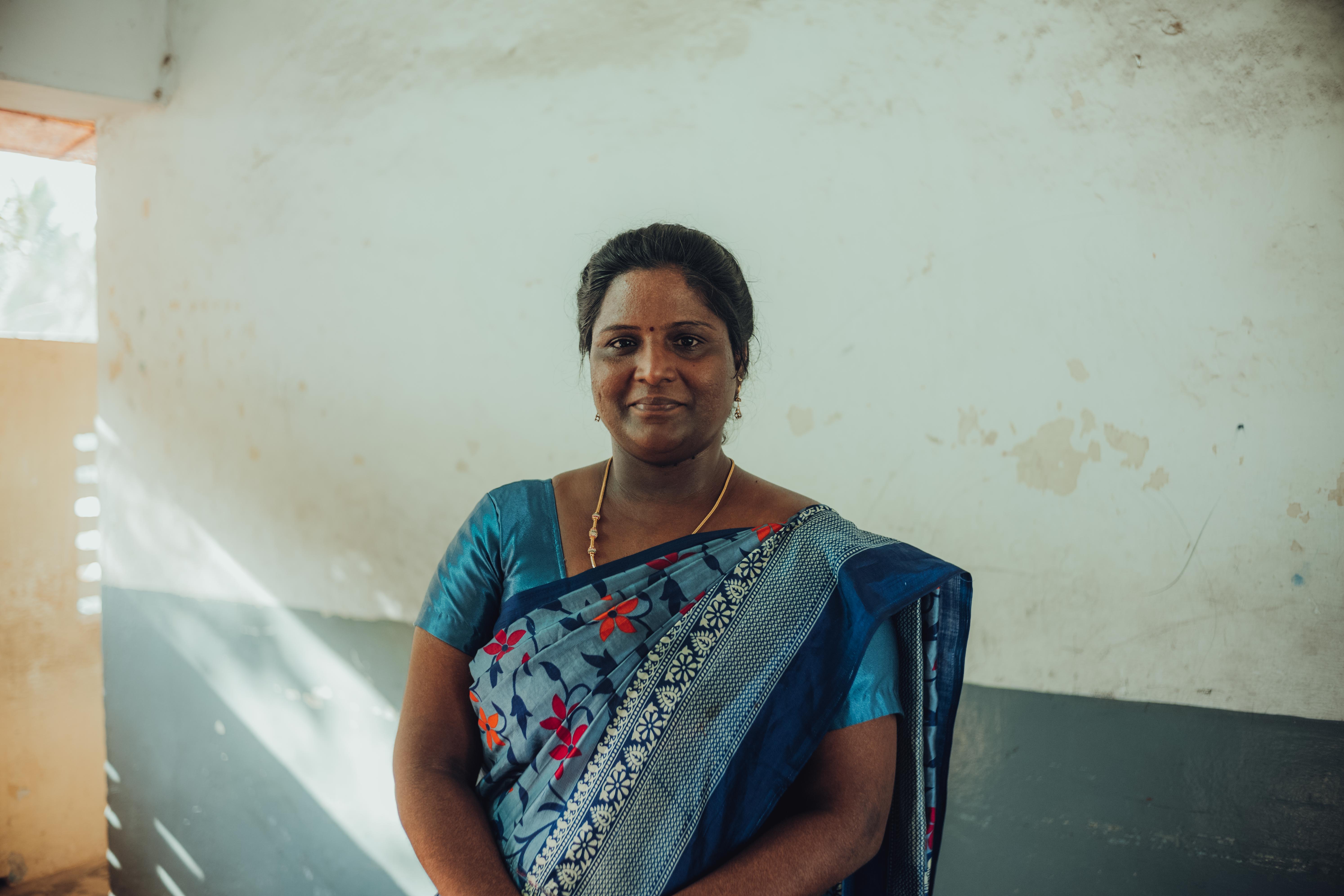 Frau in blauem Sari mit Blumenmuster steht vor alter, teils abblätternder Wand.