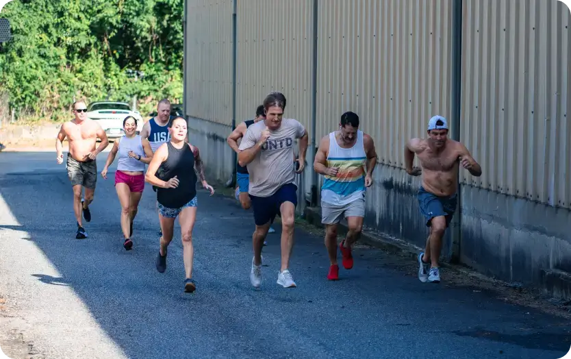 Group of seven people running outdoors on a paved path beside a building, with greenery in the background.