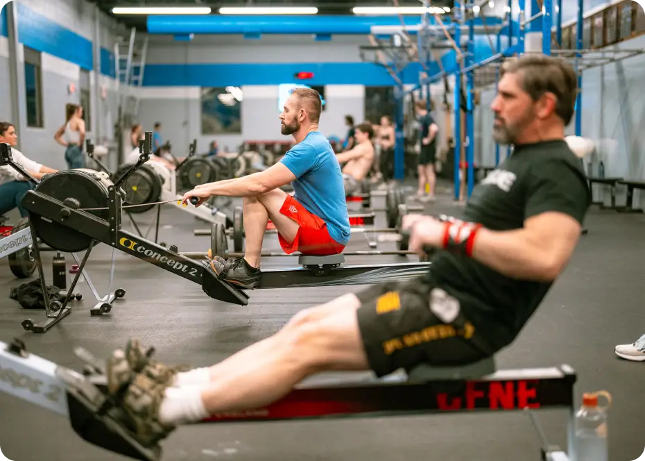 Men exercising on rowing machines in a gym with blue and white walls.