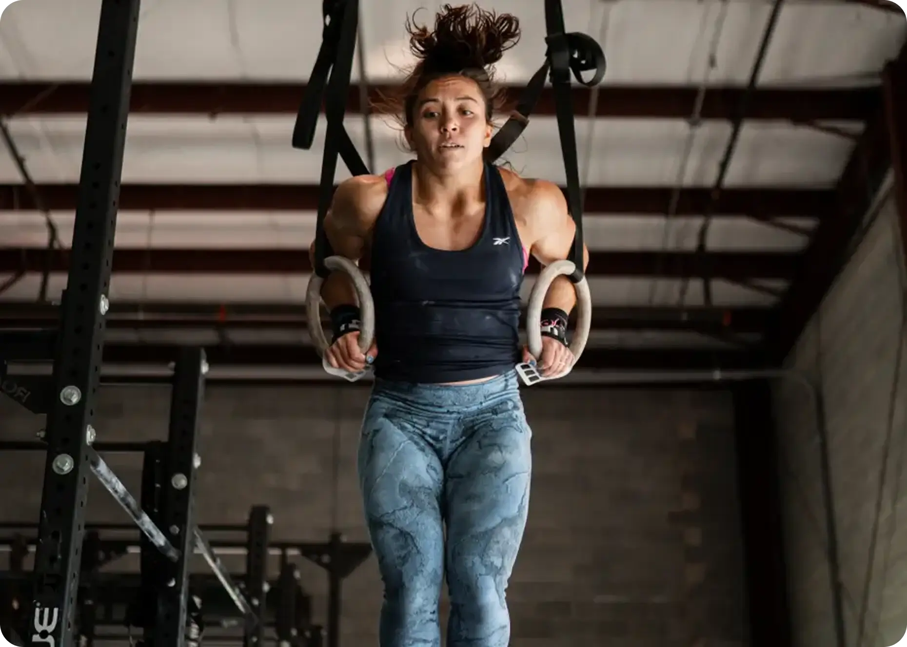 Woman performing a gymnastic ring dip exercise in an industrial-style gym.