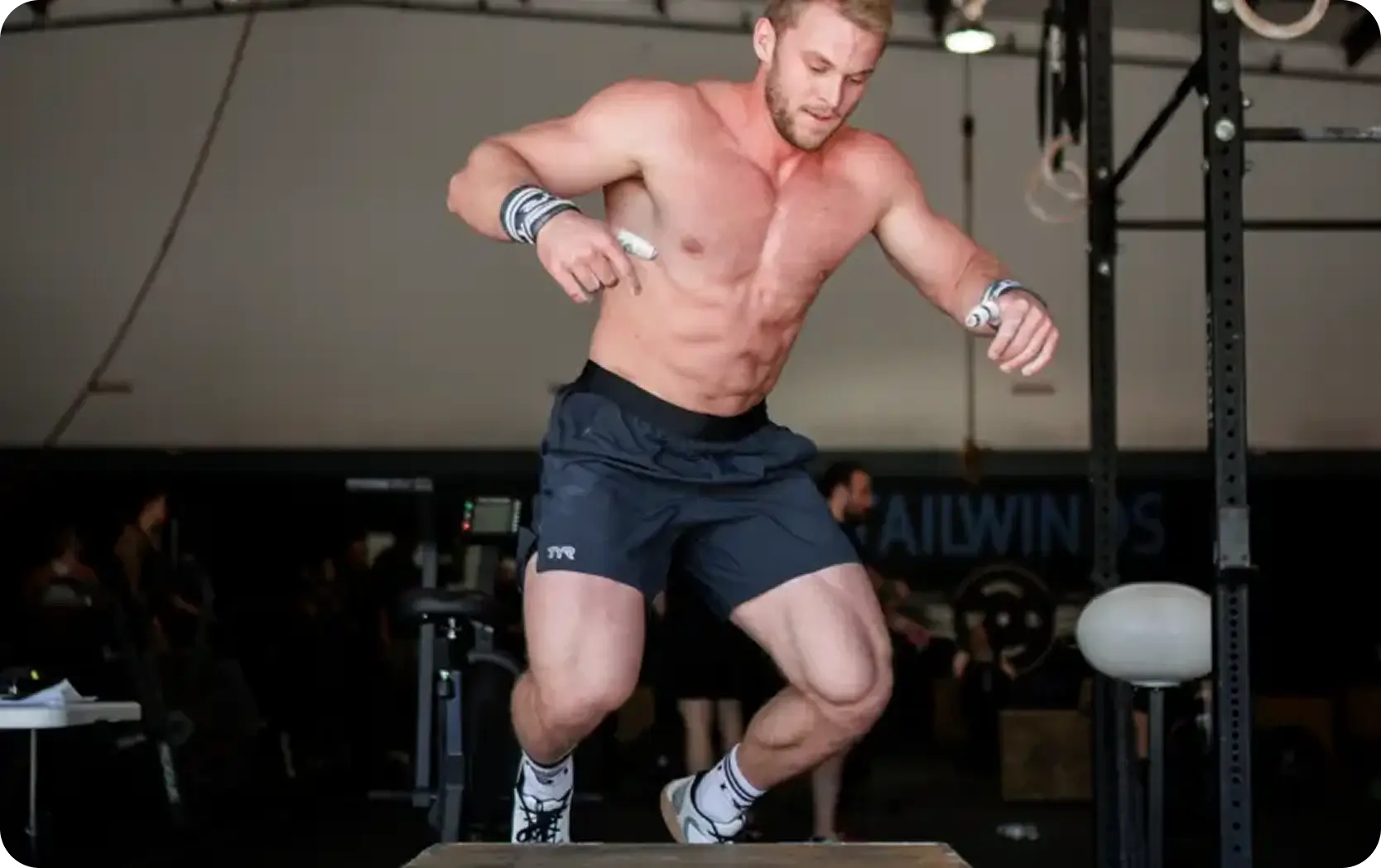 Muscular shirtless man performing a box jump exercise in a gym.