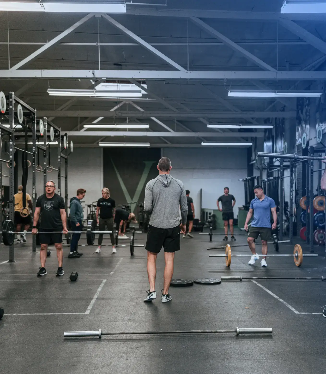 People lifting weights and exercising in a spacious gym with racks and barbells.