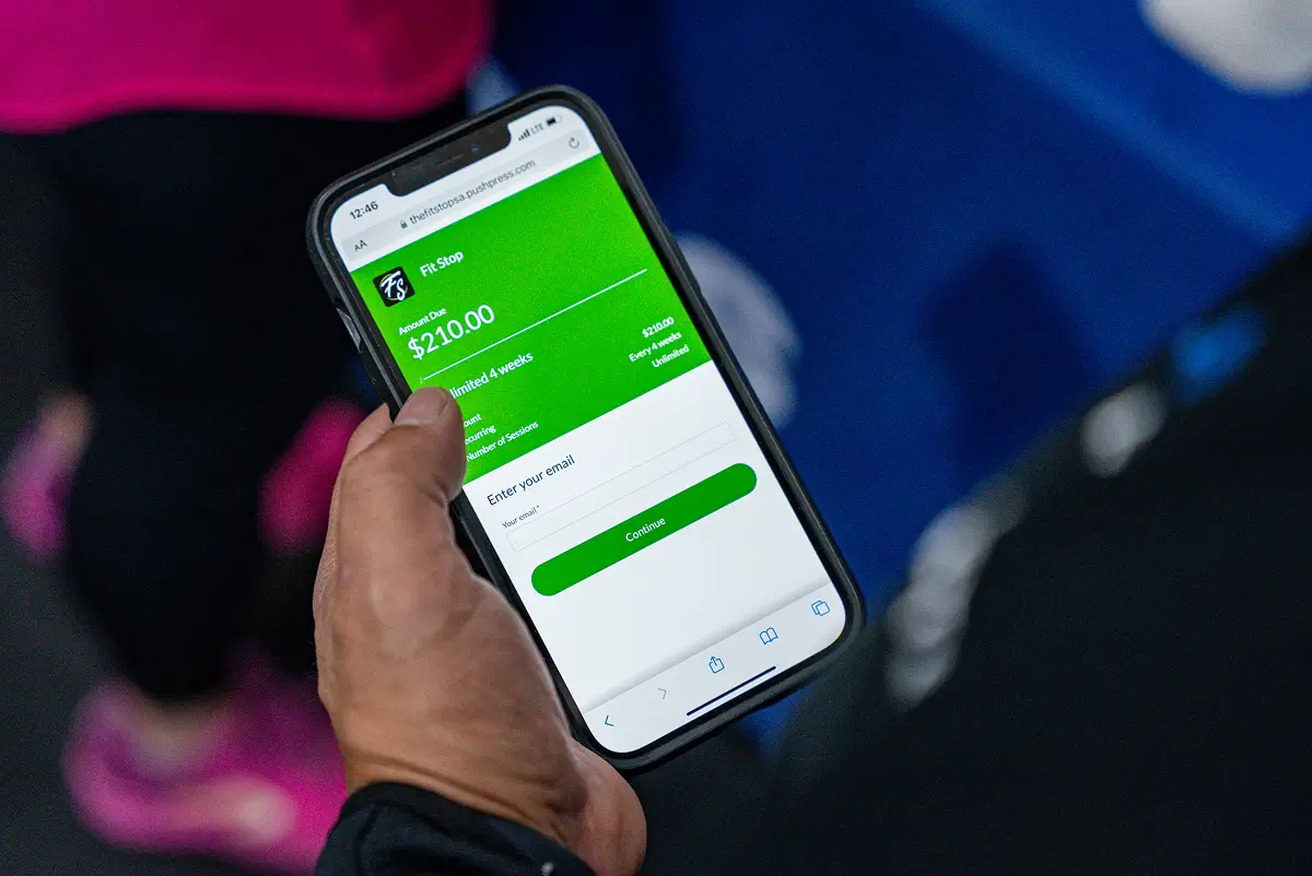 Person holding a smartphone displaying a green payment screen for Fit Stop with $210.00 amount due and email entry field.