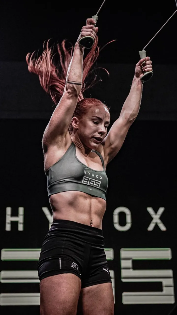 Athletic woman with red hair and a green sports bra lifting weights while her hair flows upwards.