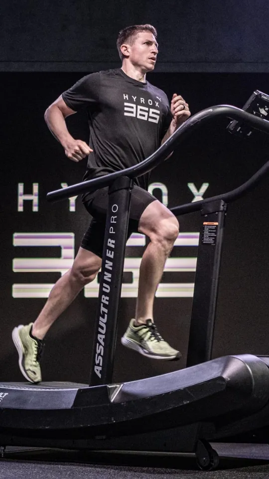 Man wearing a black HYROX 365 shirt running on an AssaultRunner Pro treadmill.