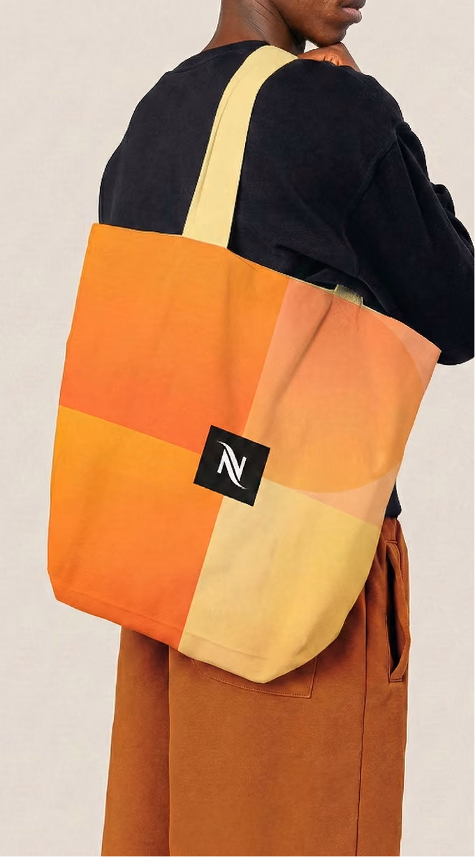 Person wearing brown pants and black shirt carrying multicolored orange and yellow tote bag with logo.