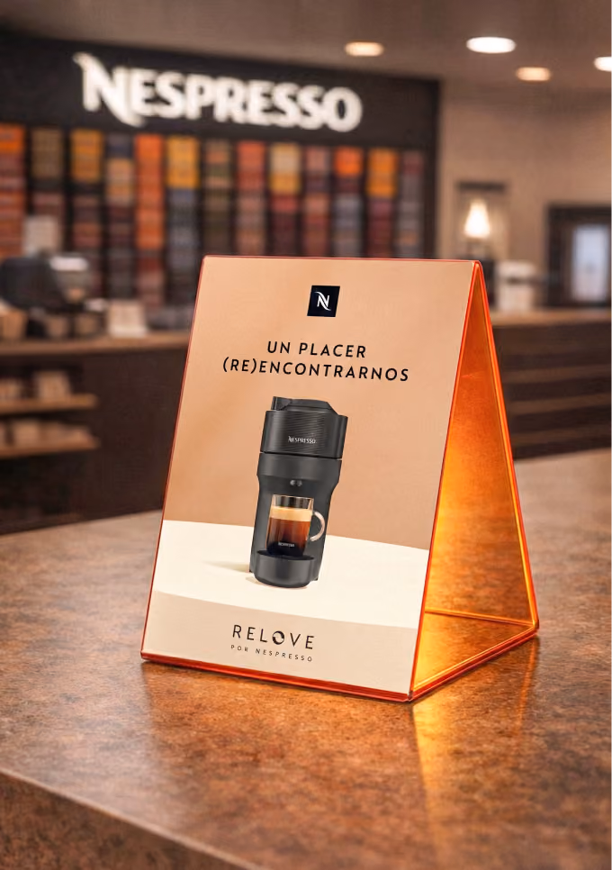 Nespresso tabletop sign with a black coffee maker and Spanish text in a store setting.